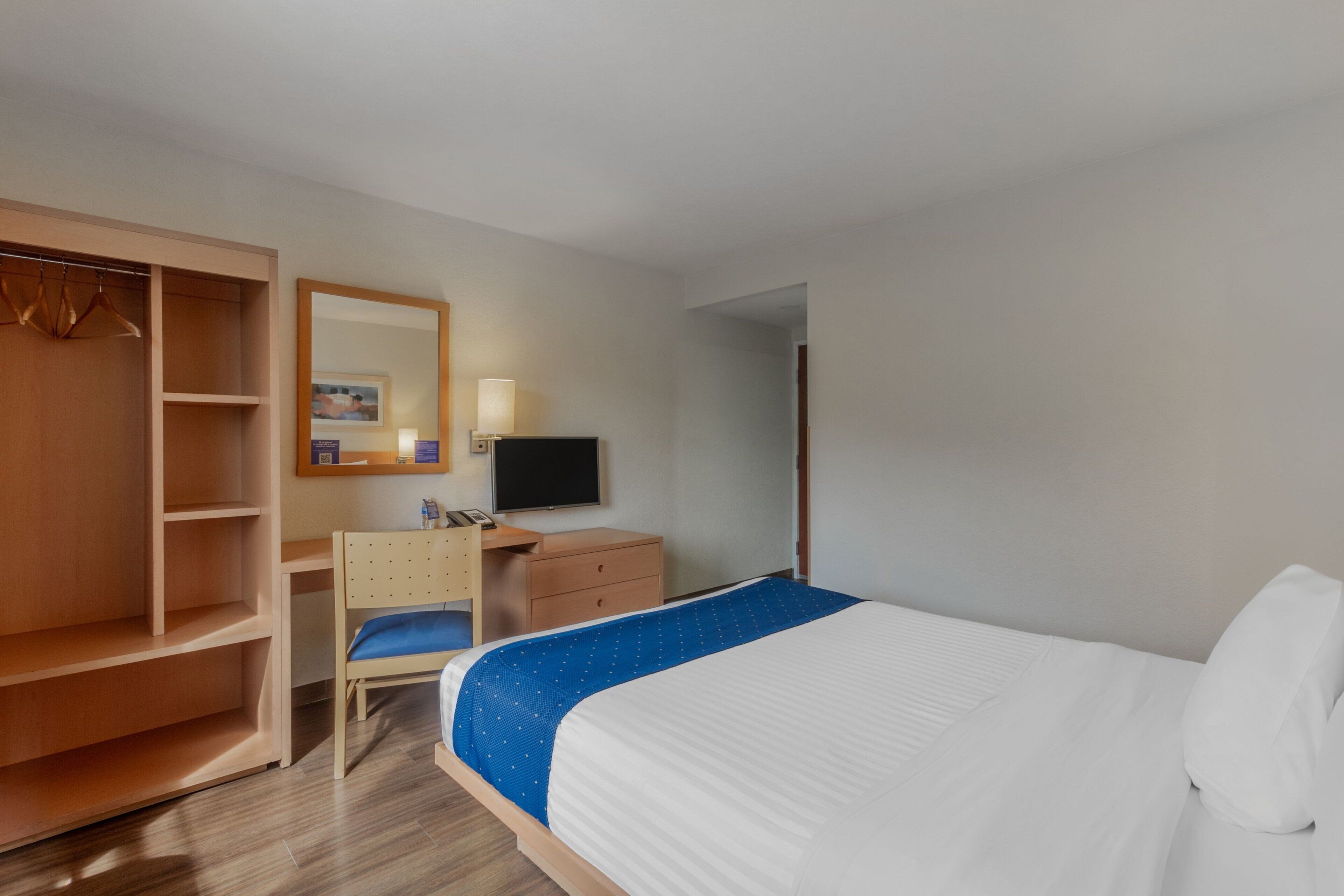 Una habitació d'hotel amb llit, escriptori, cadira, armari, televisió i mirall.