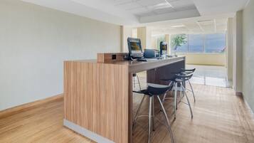 Zona de recepción con mostrador de madera, dos monitores de computadora y tres taburetes de bar.