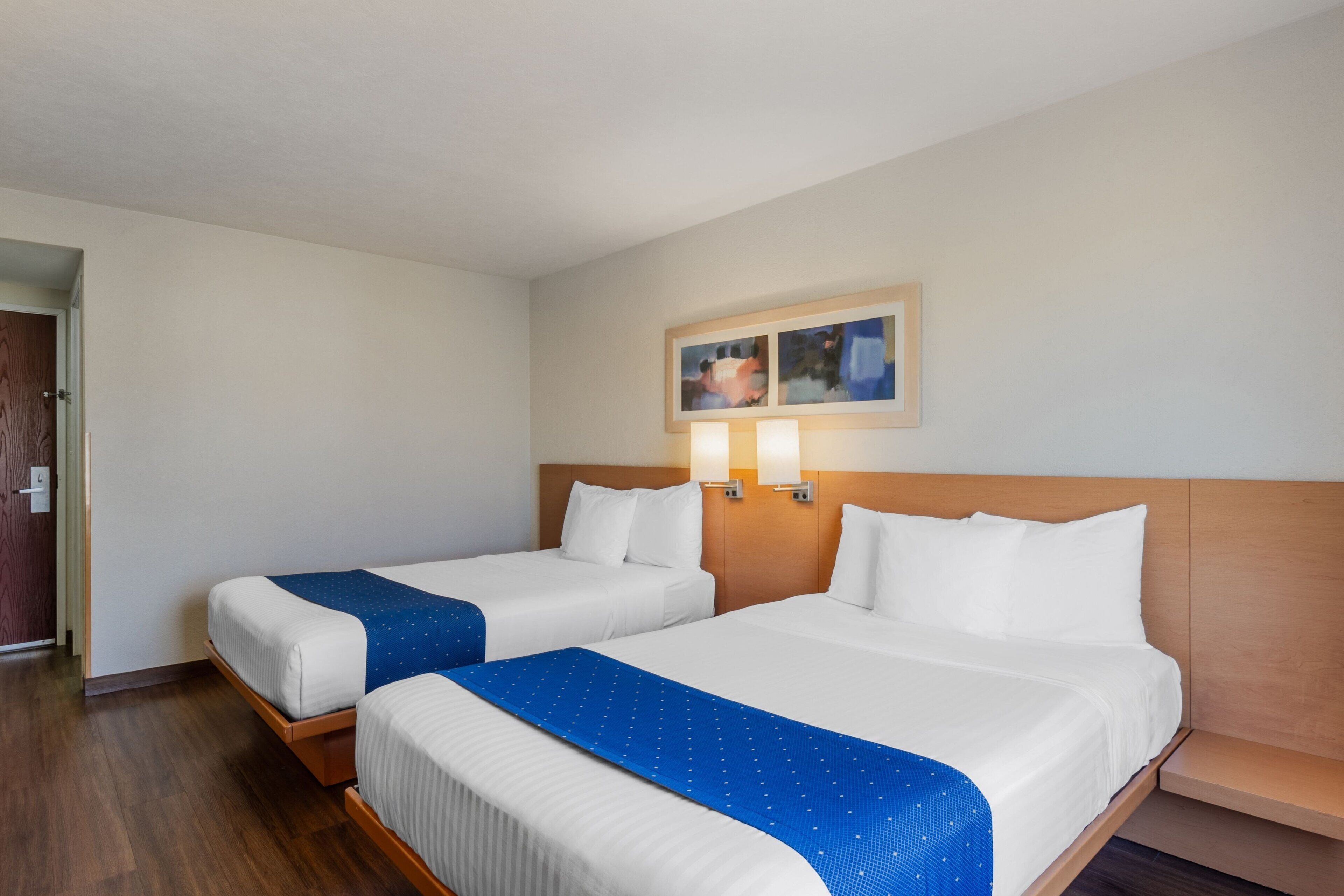 Habitació d'hotel amb dos llits, panells de capçalera de fusta i una zona de seients petita.