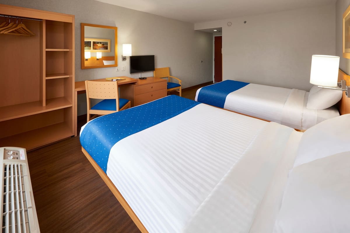 A hotel room with two beds, a desk, a chair, a TV, and a wardrobe.