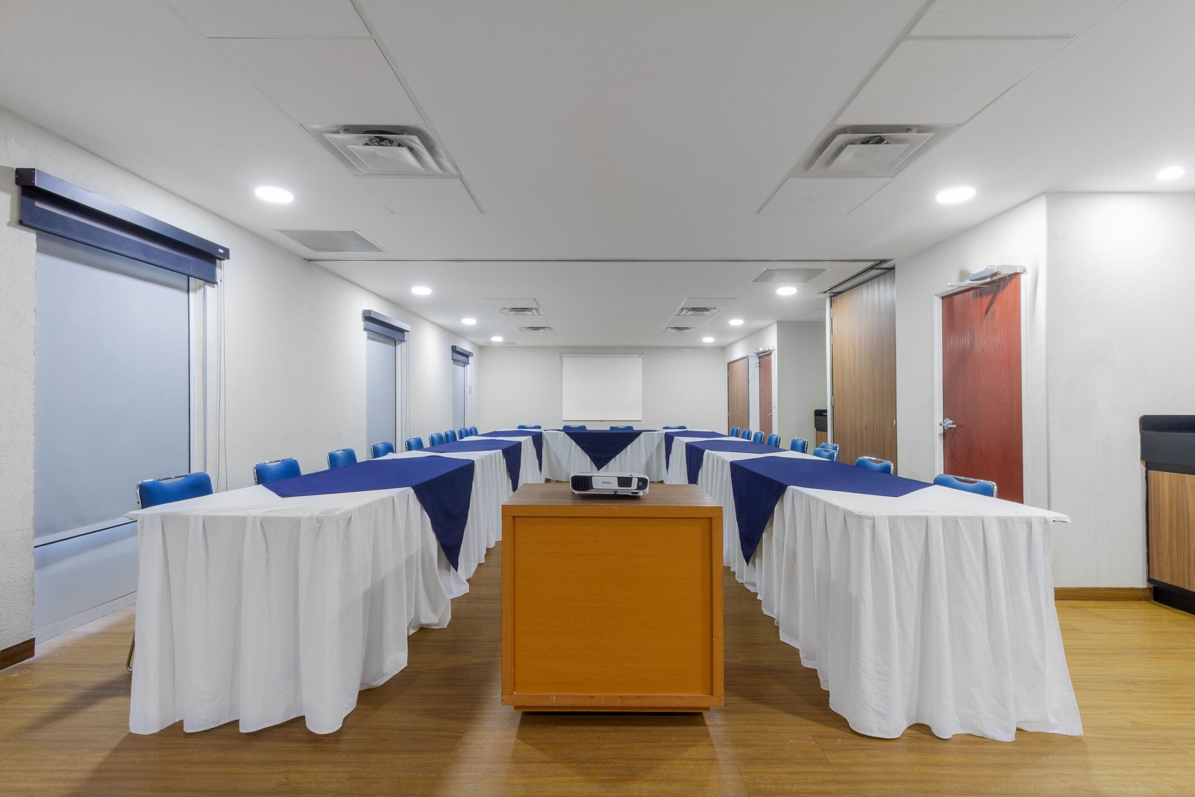 A conference room with a long table, blue chairs, white tablecloths, and a podium.