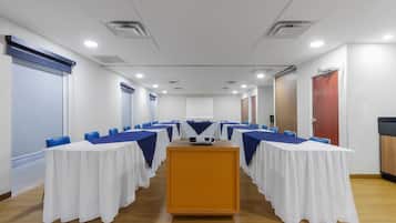 A conference room with a long table, blue chairs, white tablecloths, and a podium.