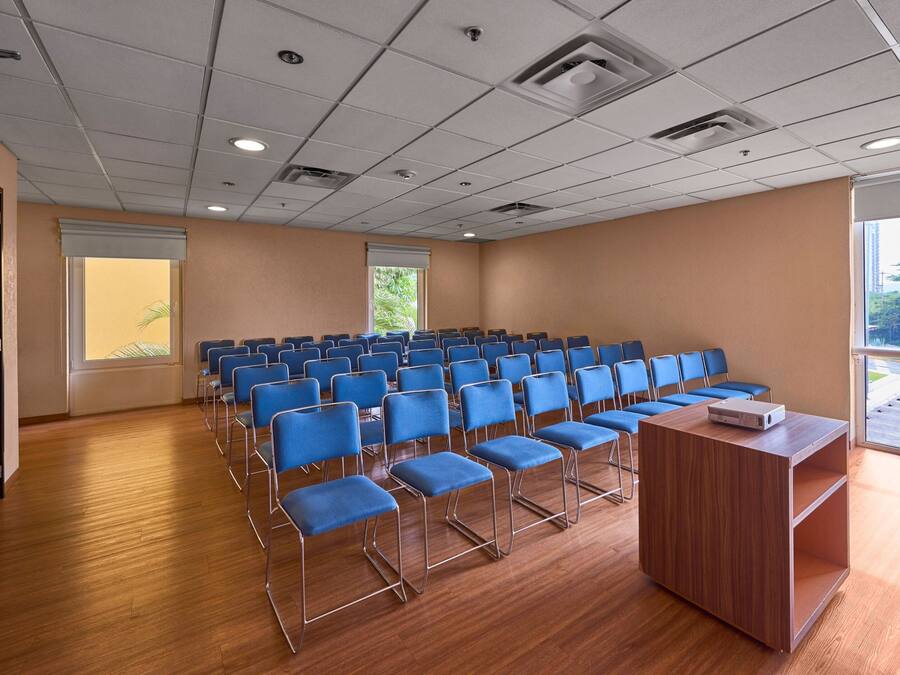 A conference room with rows of blue chairs, a wooden podium, and a large window with a view of greenery.