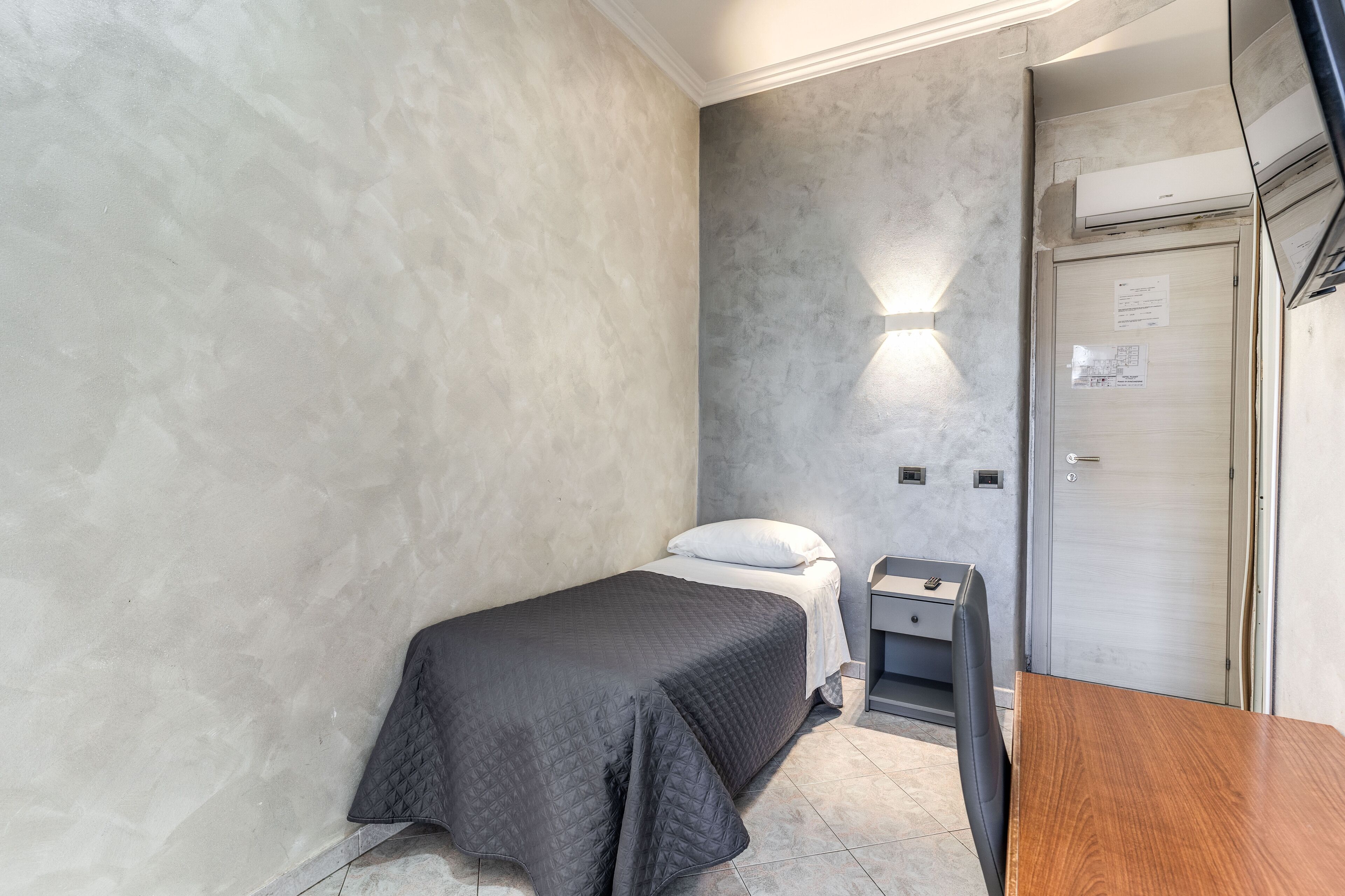 A small, modern bedroom with a single bed, a wooden table, and a nightstand.