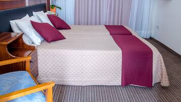 A hotel room with a large bed, two pillows, a wooden nightstand, a chair, a TV, and a potted plant.