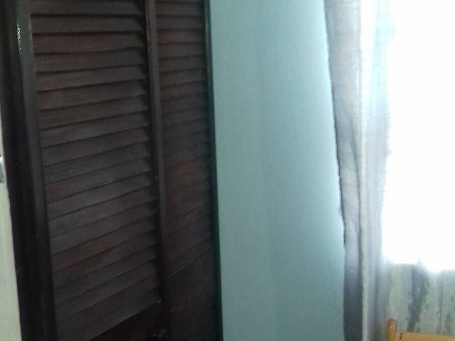 Une pièce avec une porte en bois foncé, un mur bleu clair et une fenêtre avec un rideau.
