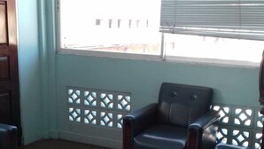 Une pièce dotée d’une grande fenêtre, d’un fauteuil, d’un canapé et d’un sol carrelé.