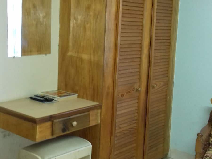 A room with a wooden wardrobe, a desk with a chair, and a small bench.