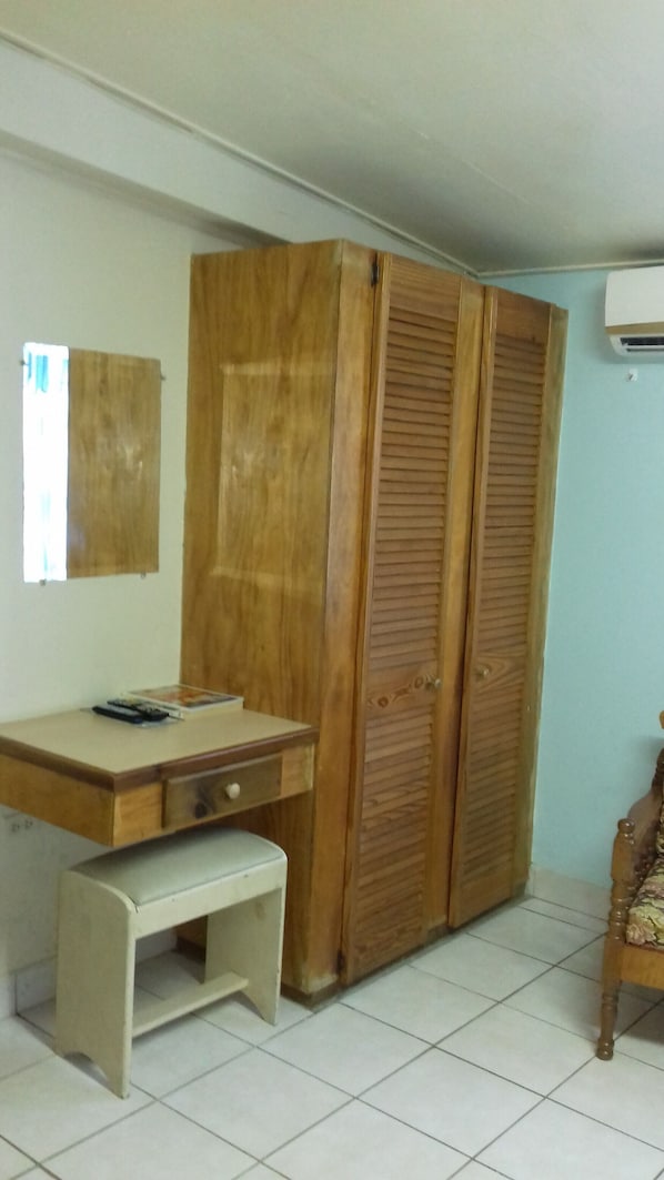 A room with a wooden wardrobe, a desk with a chair, and a small bench.