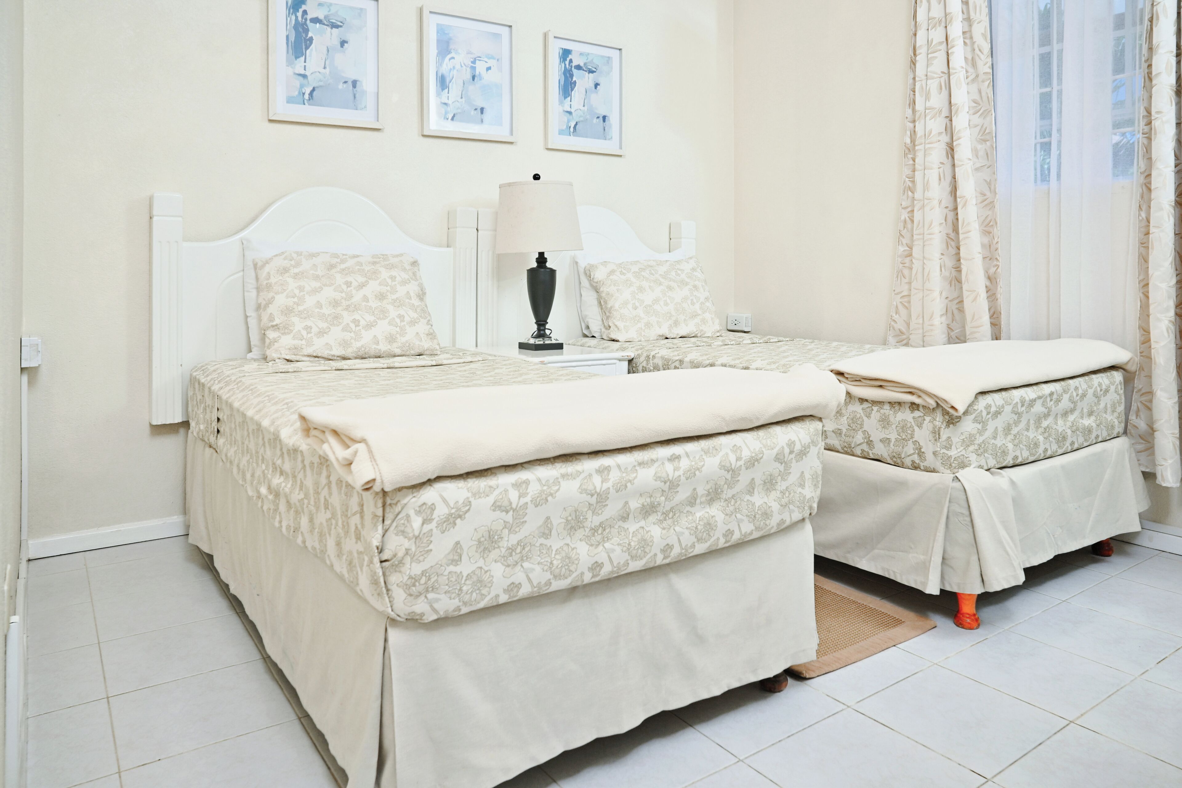 A double room with two beds, a bedside table with a lamp, and a window with curtains.