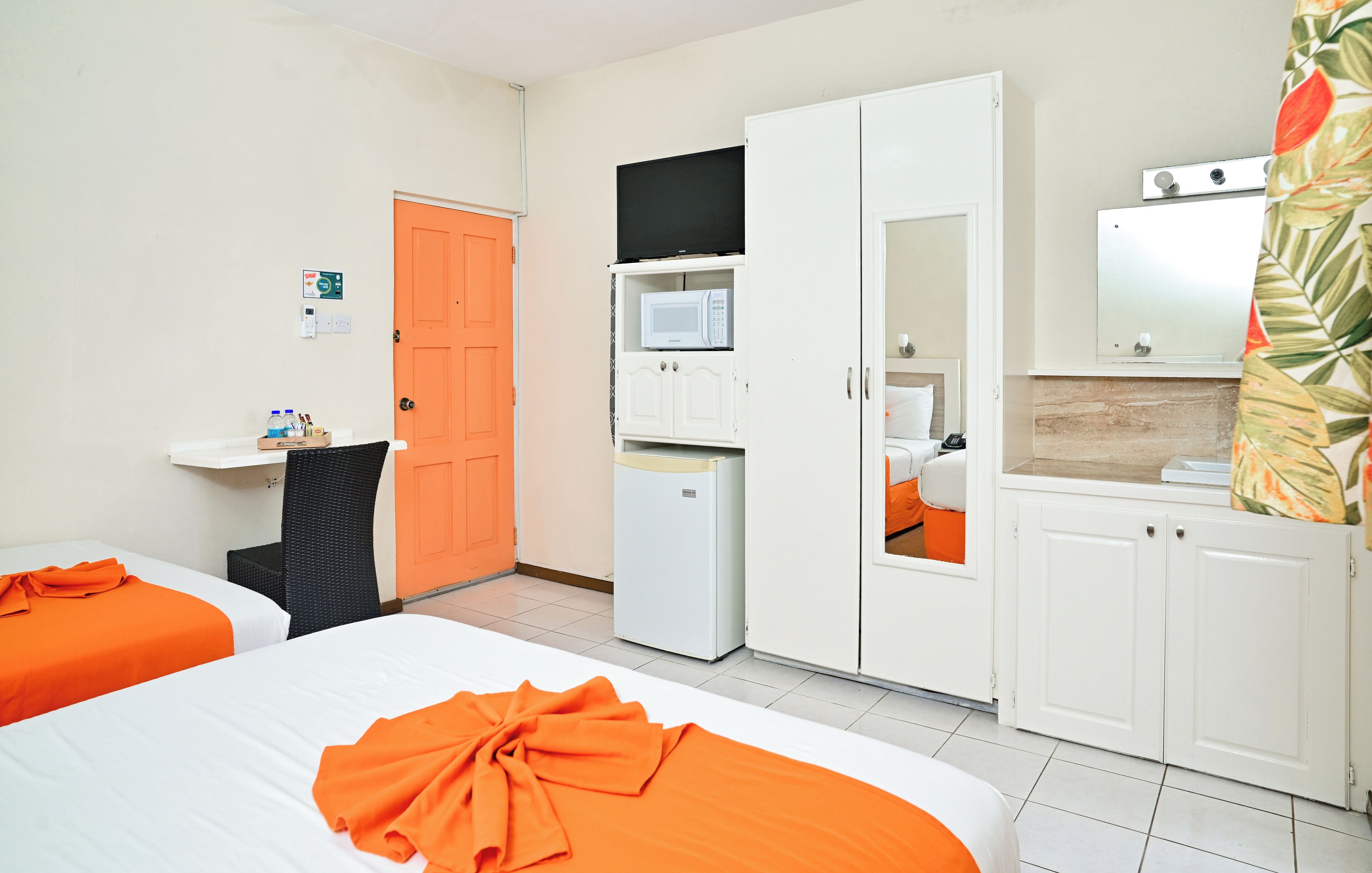 A hotel room with two beds, a microwave, a refrigerator, a television, and a bathroom visible through an open door.