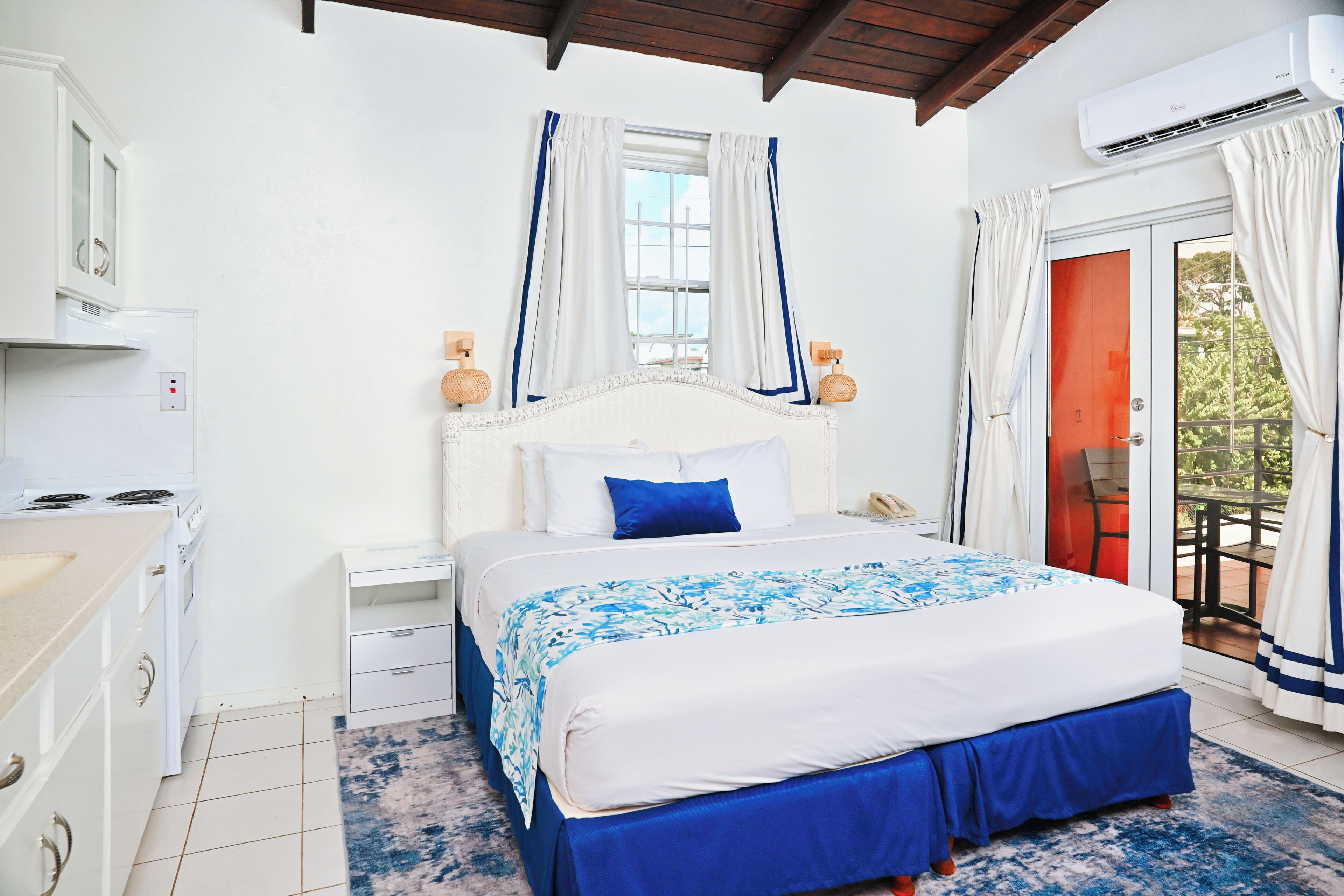 A bedroom with a bed, nightstands, a dresser, an air conditioning unit, and a view of the outdoors.