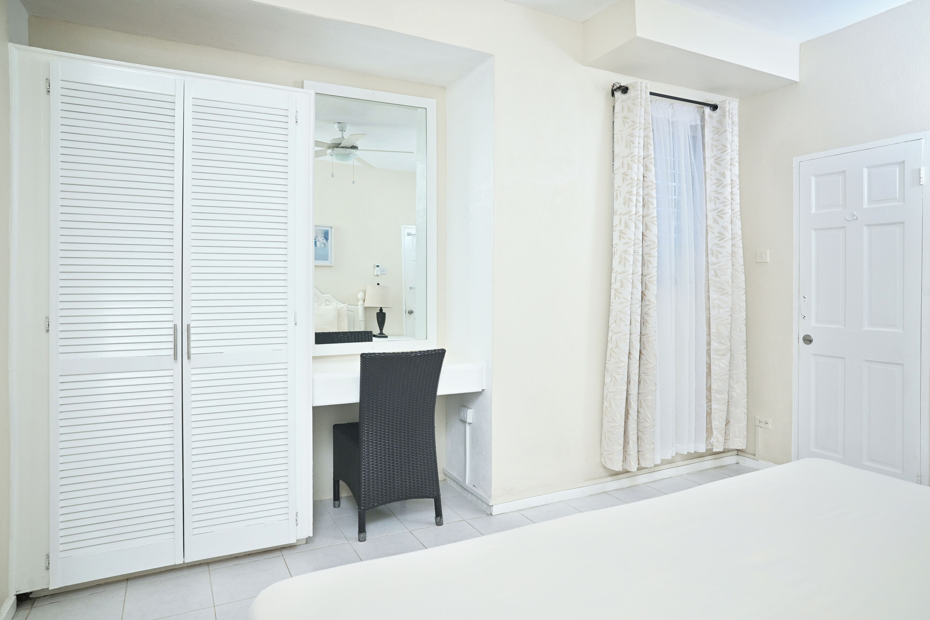 A bedroom with a bed, a desk with a chair, a wardrobe, and a shower area.