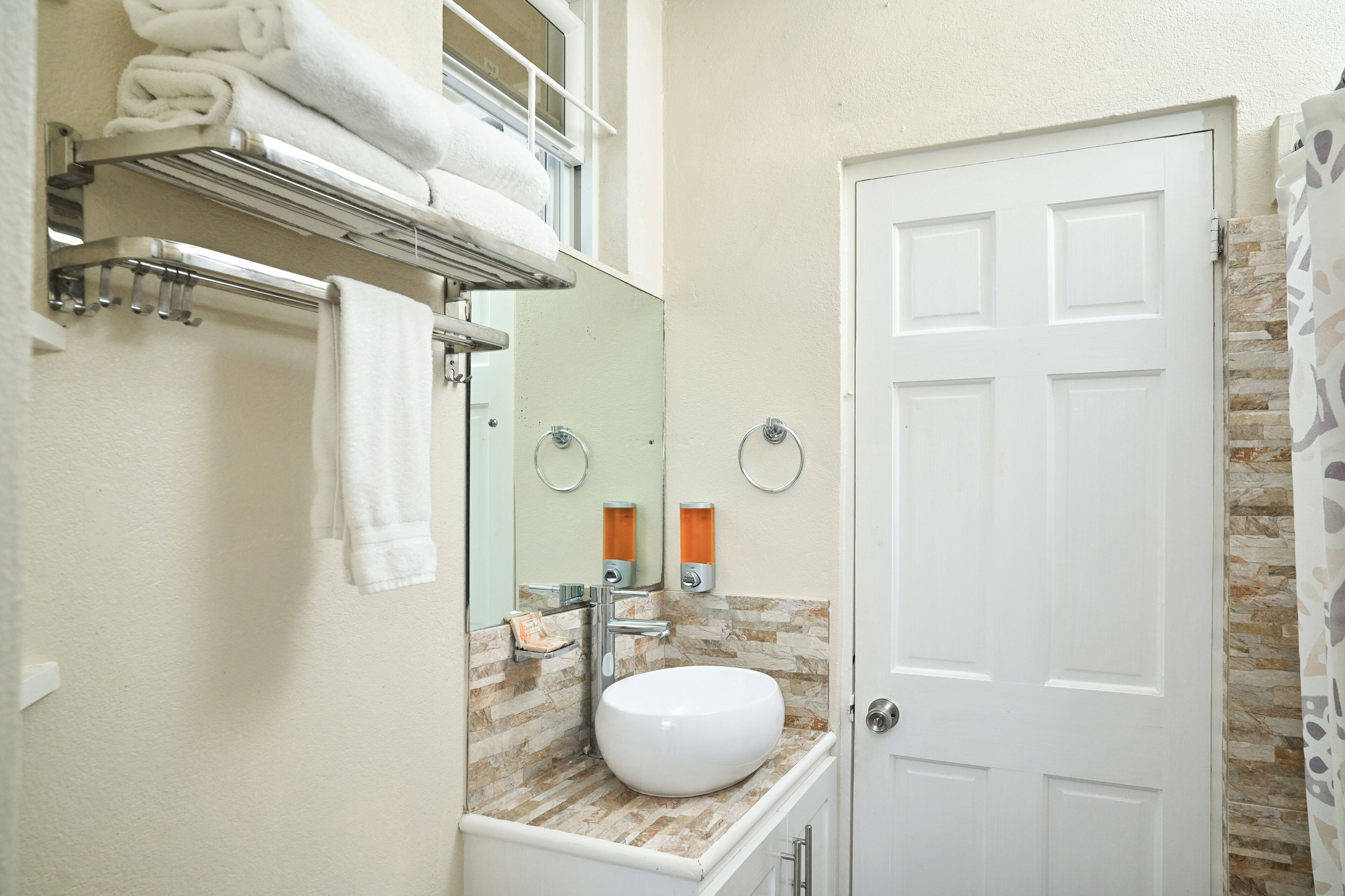 A bathroom with a white sink, a towel rack with folded towels, a mirror, and a door.