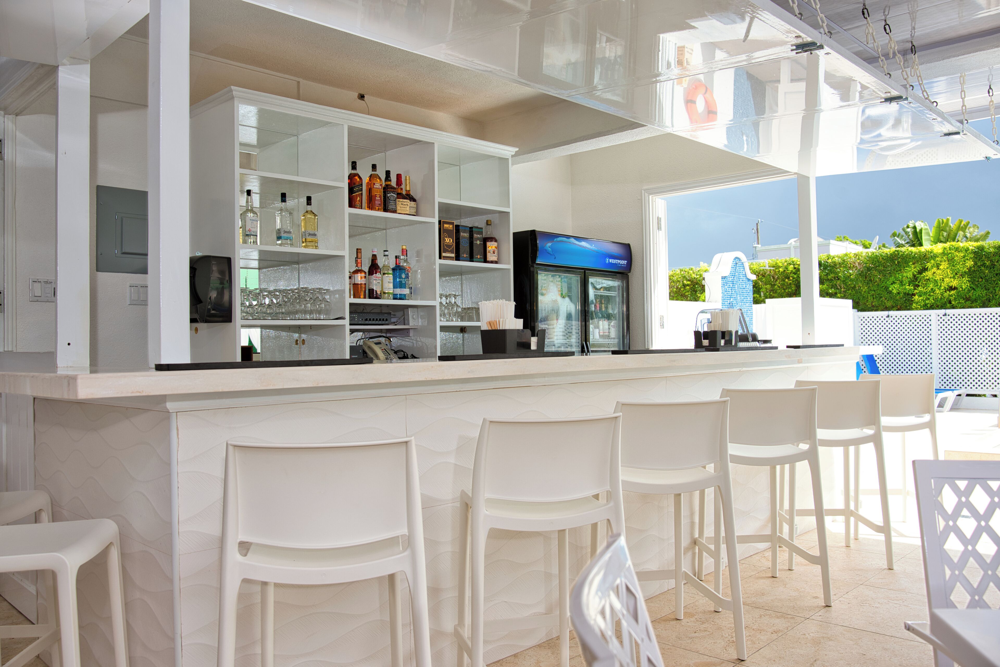 Un espace bar avec des chaises blanches, des étagères remplies de bouteilles et un réfrigérateur.
