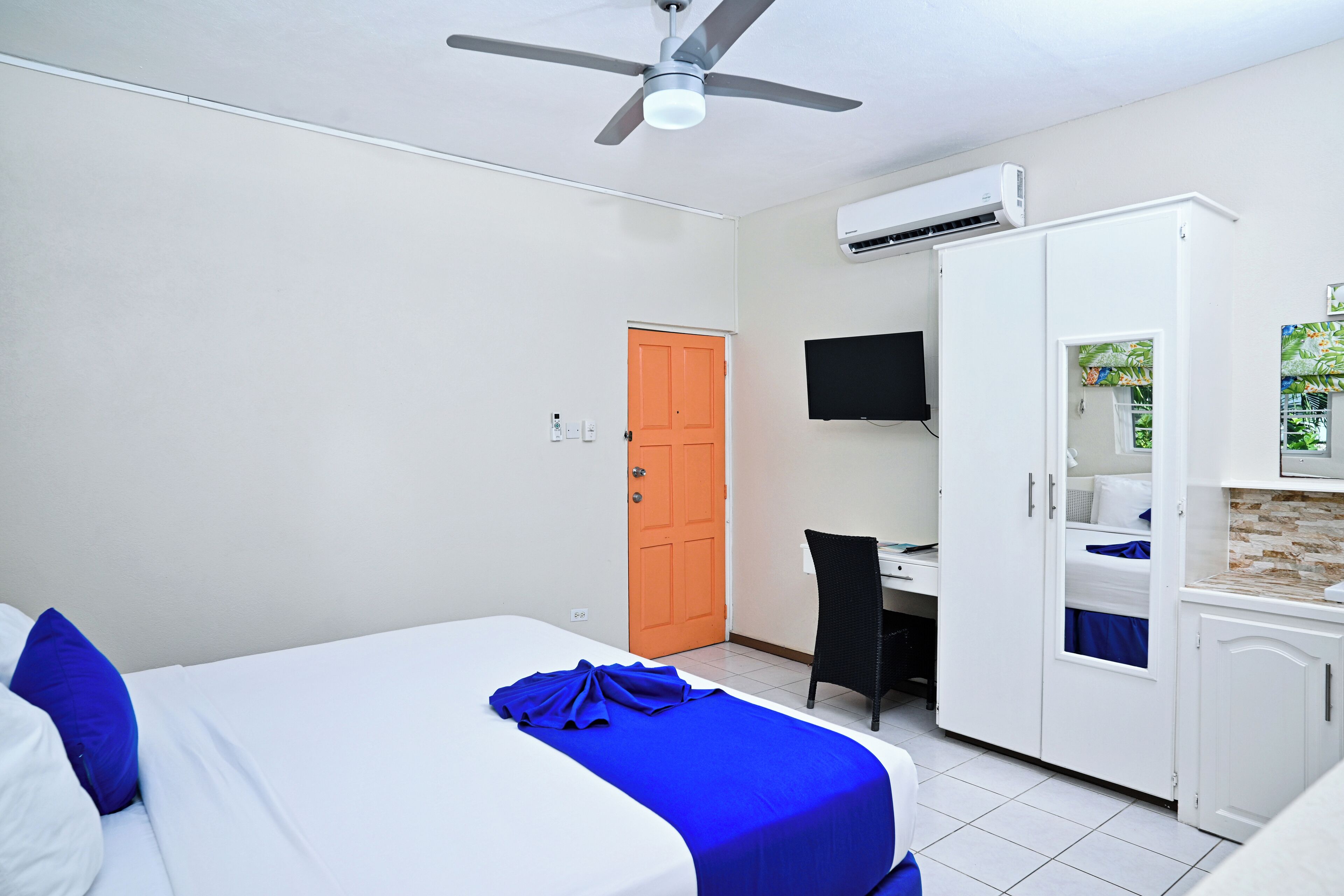 A hotel room with a bed, a desk, a chair, an air conditioning unit, and a wardrobe.