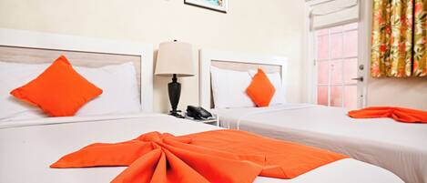 Habitación de hotel con dos camas, cada una con ropa blanca y almohadas naranjas. Hay dos cuadros en la pared, una lámpara en la mesita de noche y una ventana con cortinas.