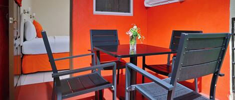 Una habitación con cama, una mesa con sillas, un florero con flores y una ventana.