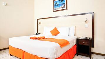 Una cama bien hecha con ropa de cama blanca y naranja, una mesita de noche con una lámpara y un cuadro en la pared.