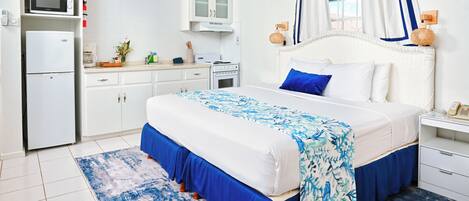 A bedroom with a bed, a nightstand, a bedside table, a wardrobe, a microwave, a refrigerator, and a window with curtains.