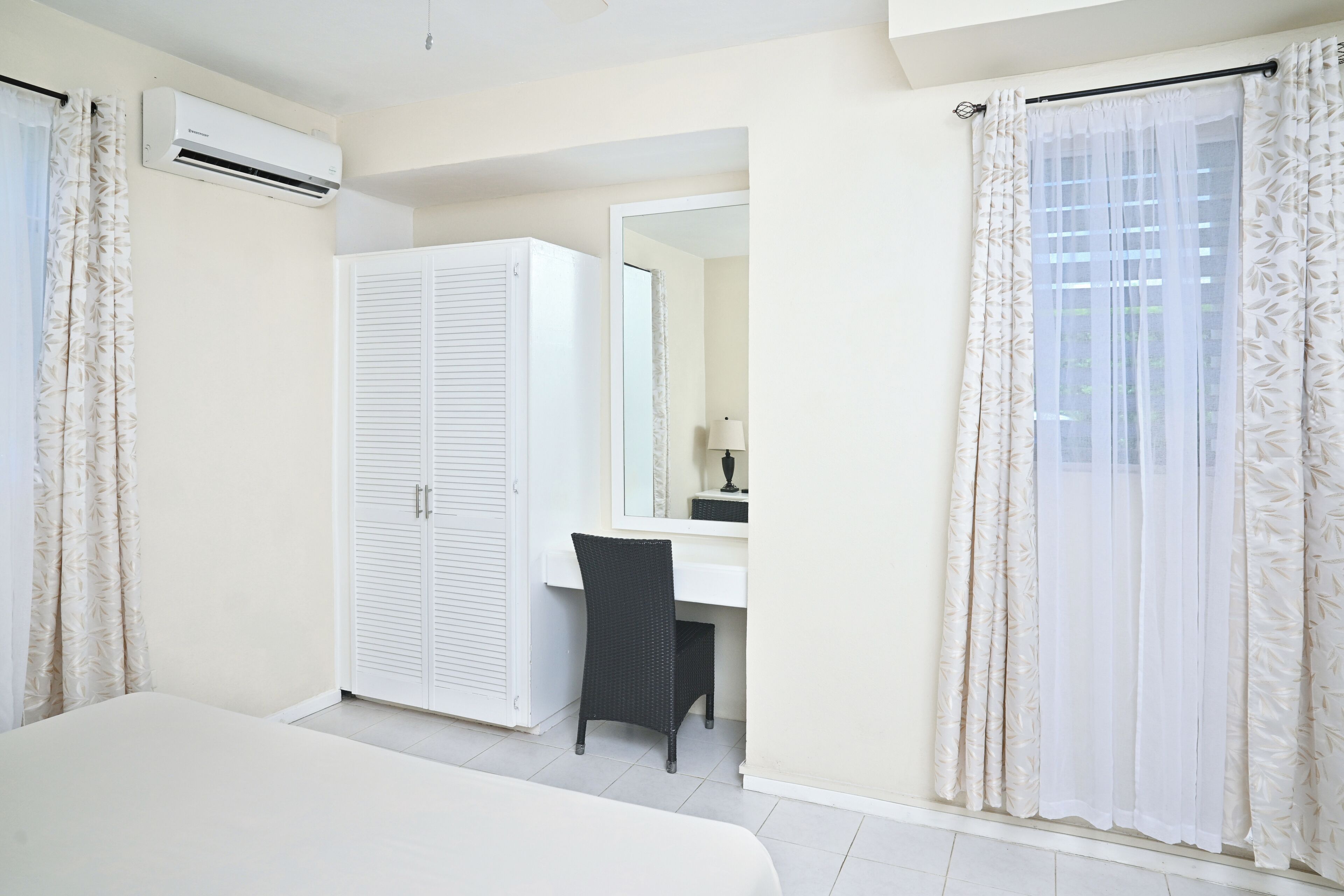 A bedroom with a bed, a desk, a chair, a wardrobe, and a bathroom mirror.