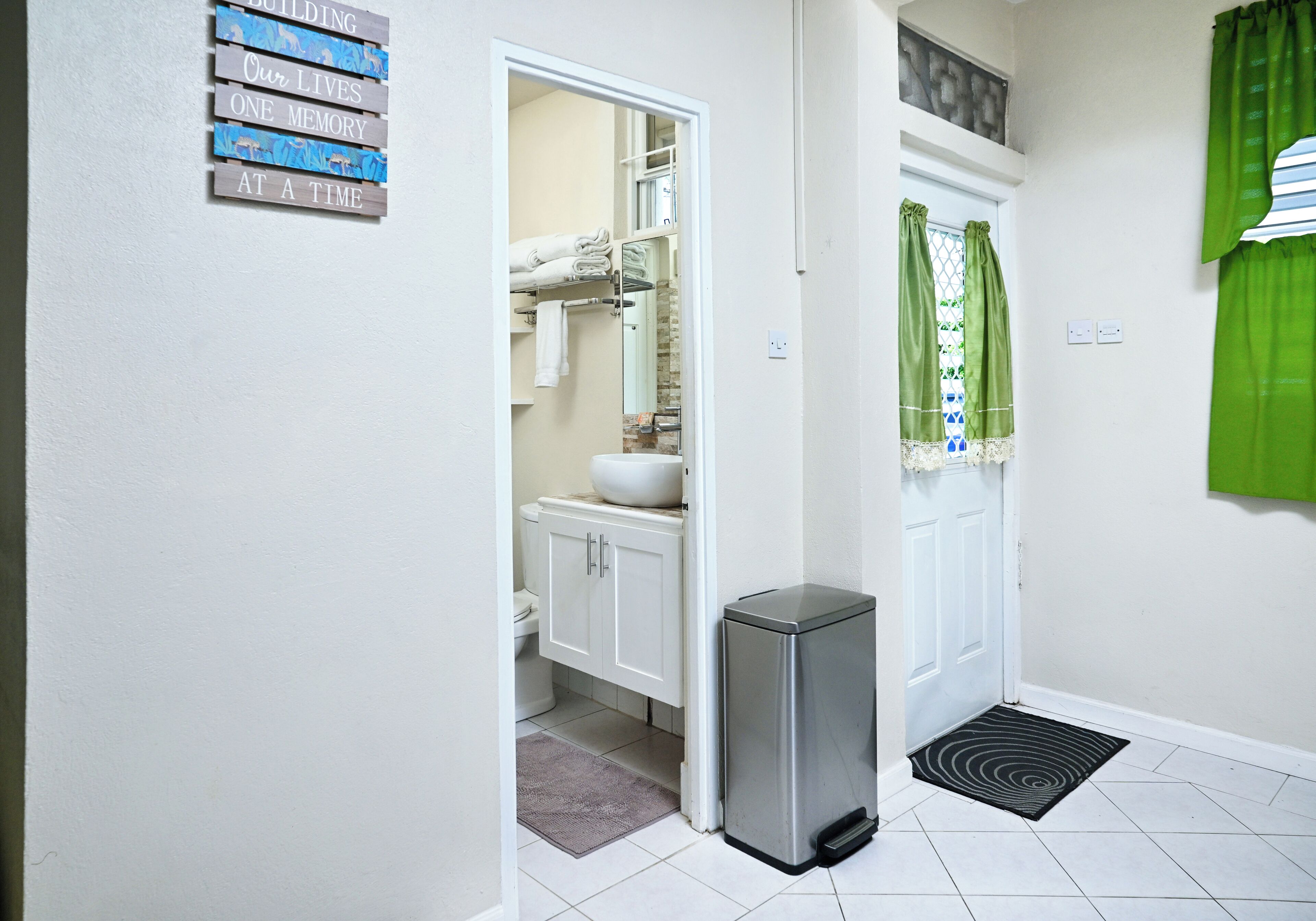 A bathroom with a toilet, sink, and storage cabinet. There is a trash bin and a green curtain.