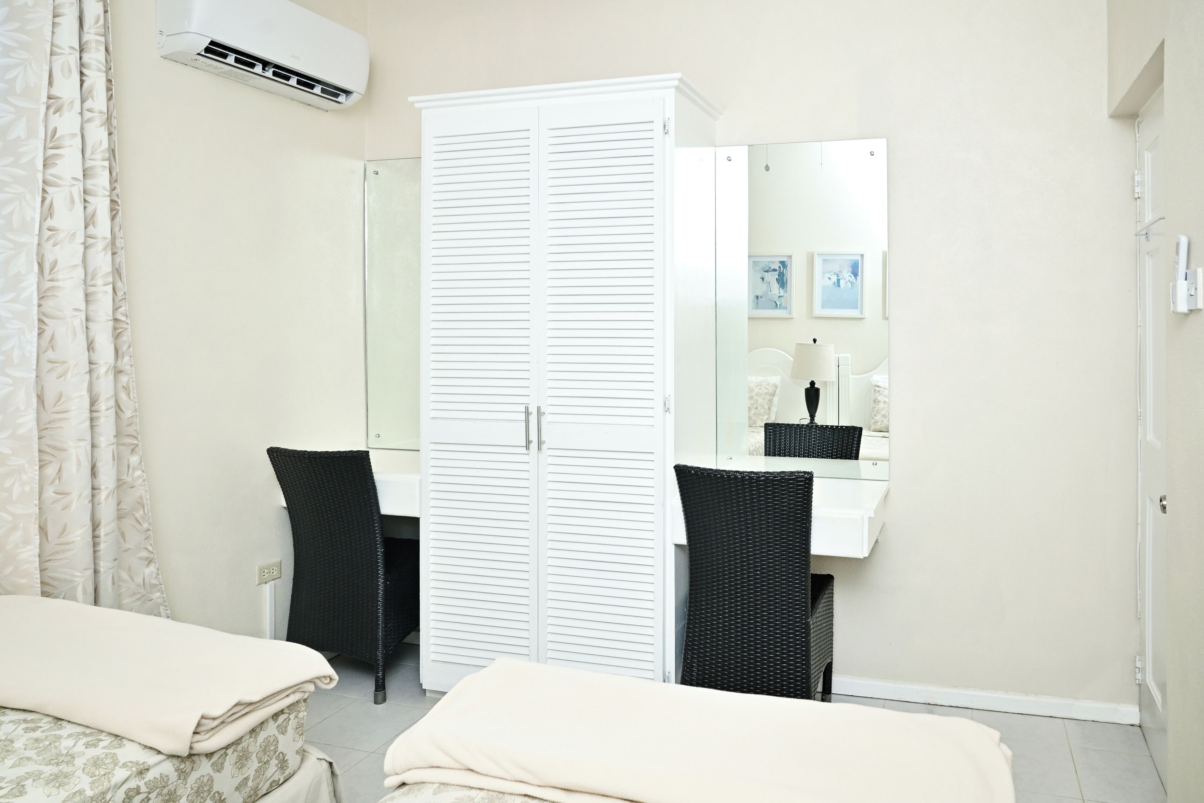 A bedroom with a bed, a wardrobe, a desk with a chair, a mirror, and an air conditioning unit.