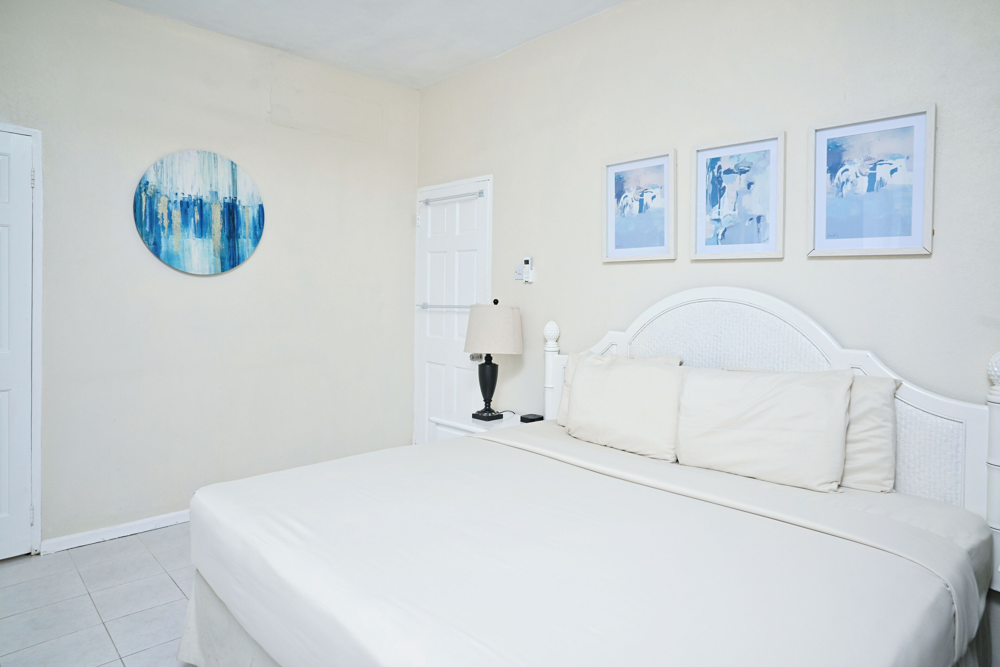 A bedroom with a bed, a round painting, and three framed pictures on the wall.