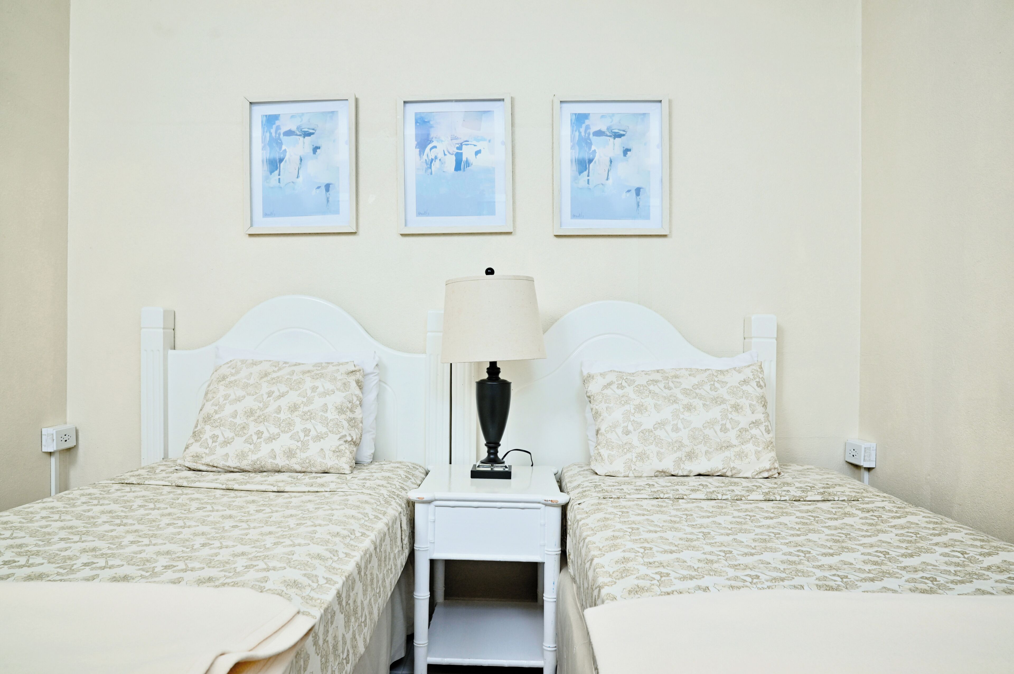 A double room with two beds, a nightstand with a lamp, and three framed pictures on the wall.