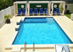 Una piscina al aire libre, sombrillas, sillones reclinables de piscina