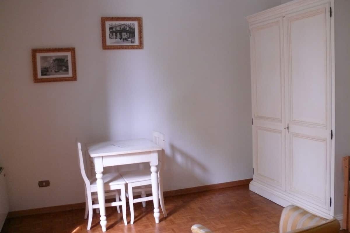 Ein Zimmer mit einem weißen Tisch, Stühlen, einem Kleiderschrank und zwei gerahmten Bildern an der Wand.