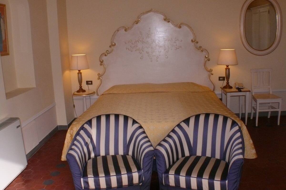 Ein Hotelzimmer mit einem großen Bett, zwei gestreiften Sesseln, einem runden Spiegel und zwei Nachttischlampen.