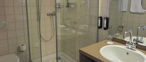 Un baño moderno con ducha envuelta en vidrio, un lavabo blanco y un espejo grande.