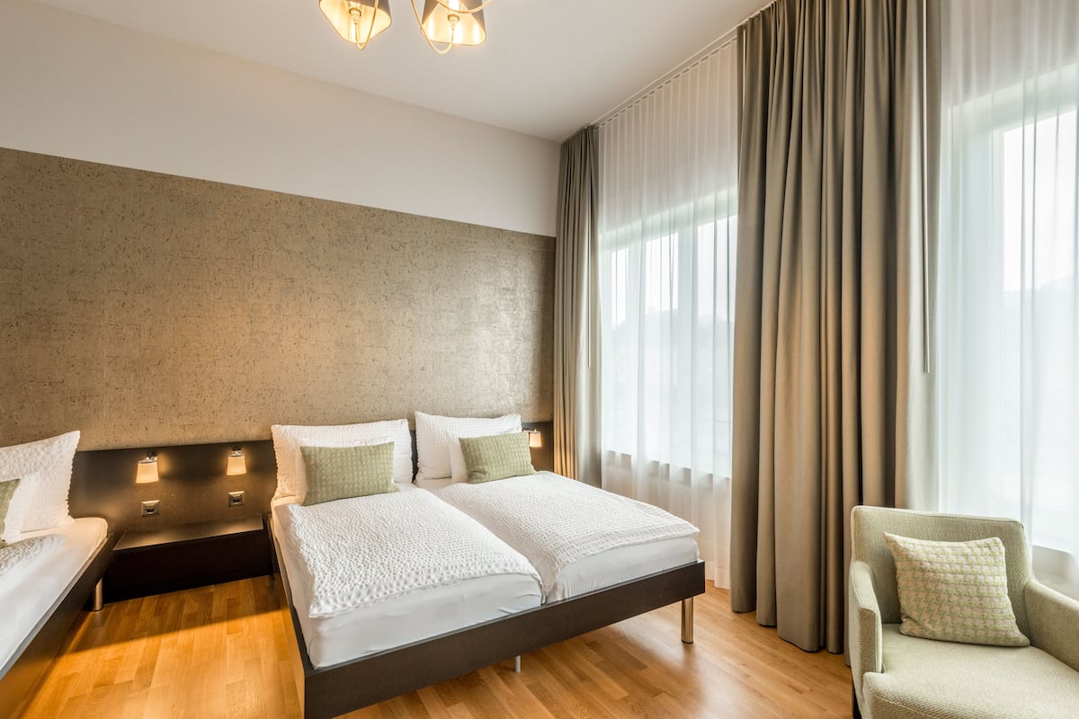 A hotel room with a large bed, two bedside tables, a chair, and a large window with curtains.