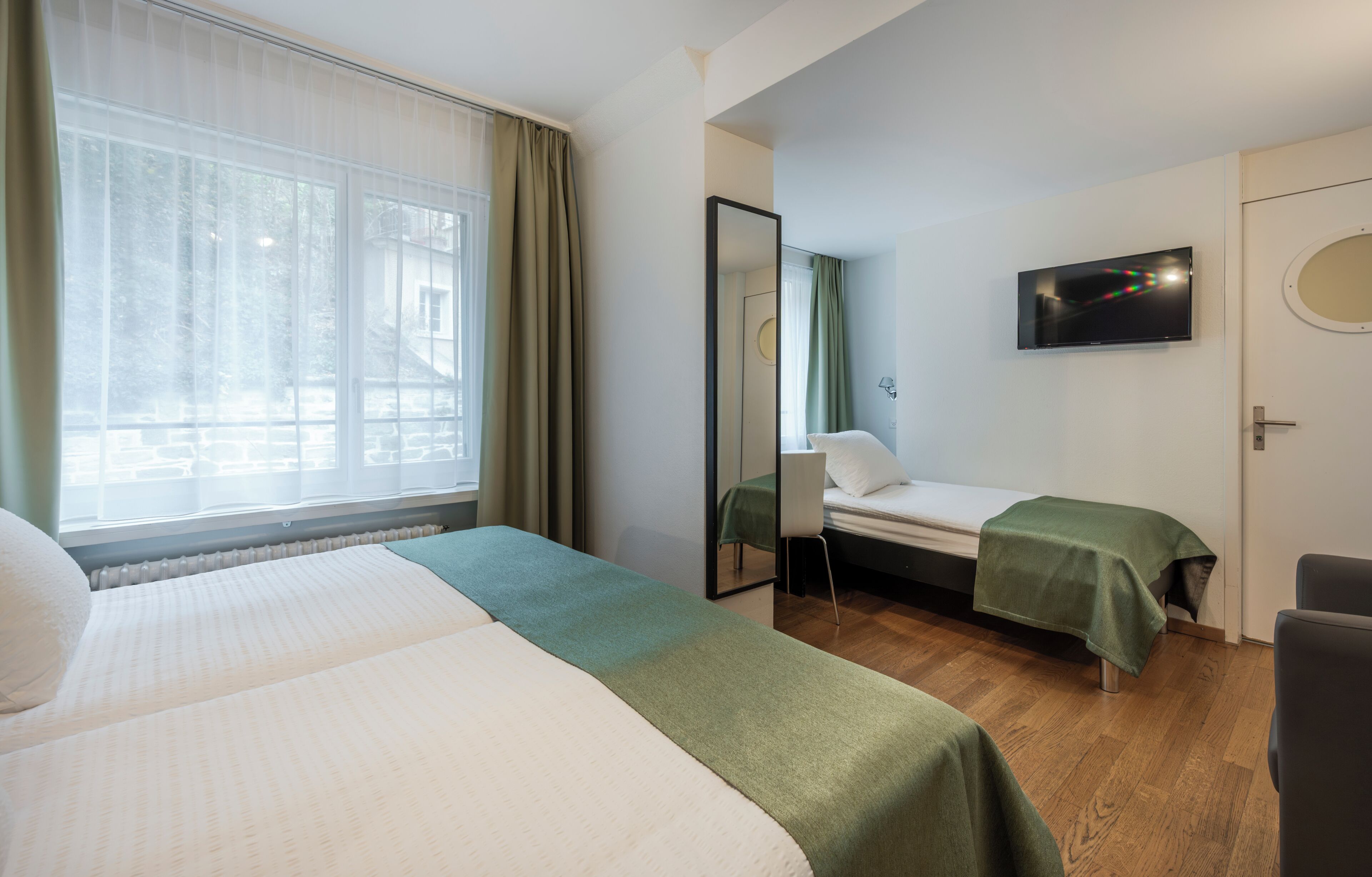 A hotel room with two beds, a television, a mirror, and a window with curtains.