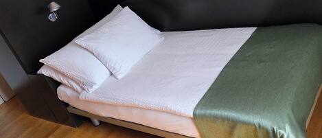 A single bed with a white mattress and pillows, a green blanket, and a black headboard.