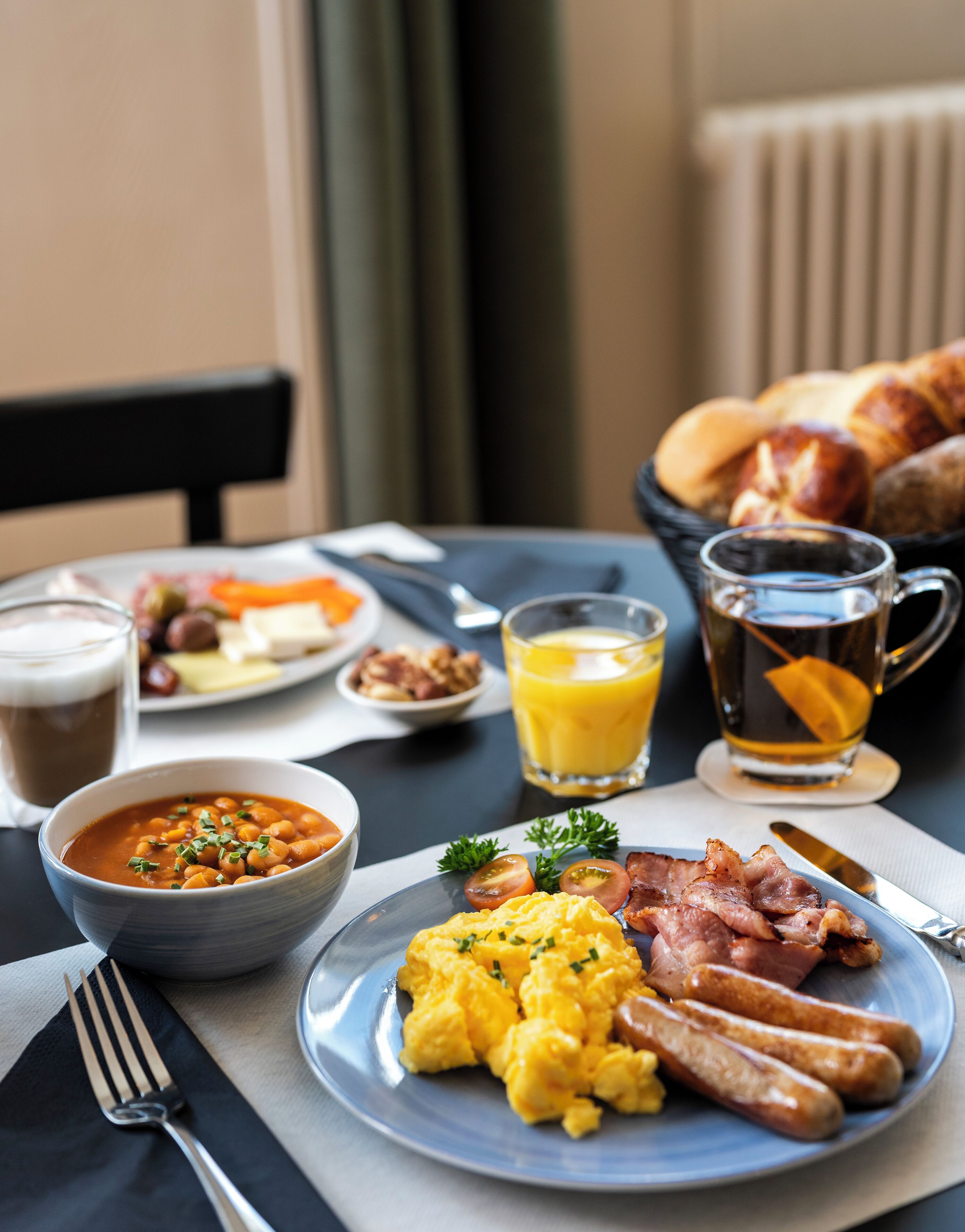 Une table de petit-déjeuner avec des œufs brouillés, des saucisses, un bol de soupe et un verre de jus d’orange.