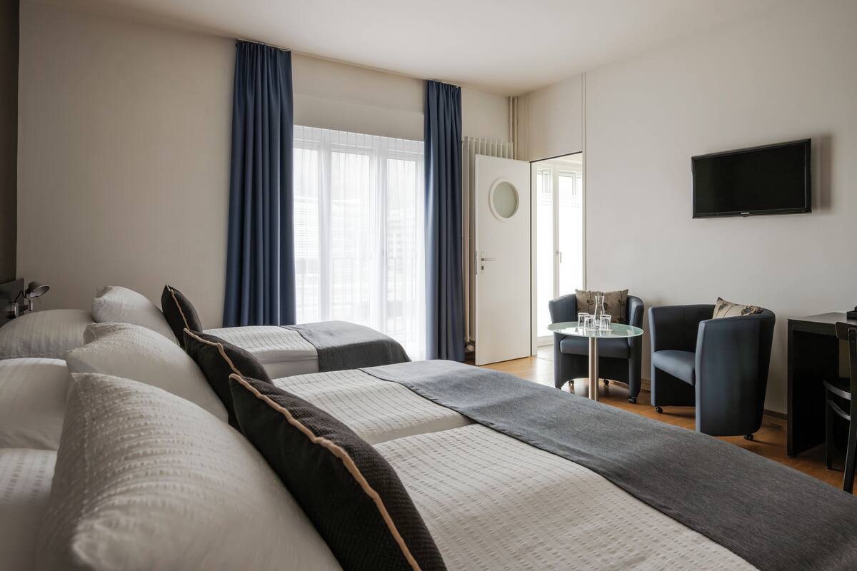 A hotel room with a large bed, a desk with a chair, a TV, and a window with curtains.