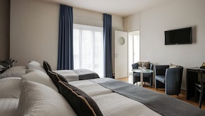 A hotel room with a large bed, a desk with a chair, a TV, and a window with curtains.