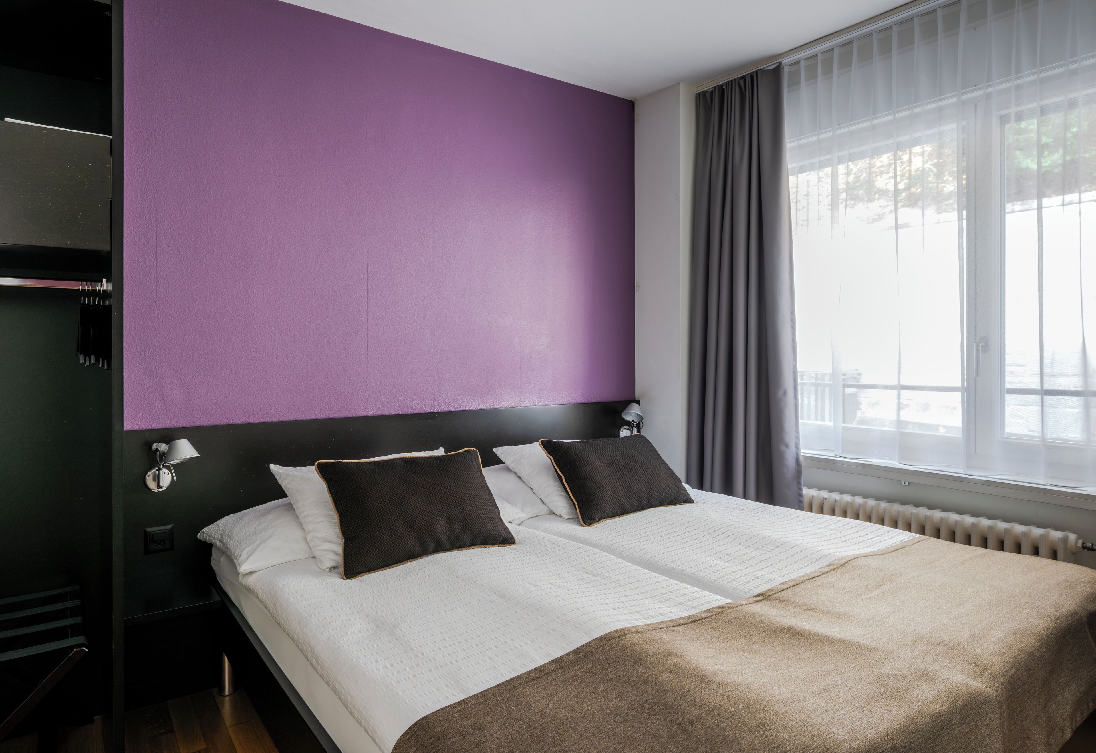 Ein Hotelzimmer mit einem Bett, einem Nachttisch, einer Lampe und einem Fenster mit Vorhängen.