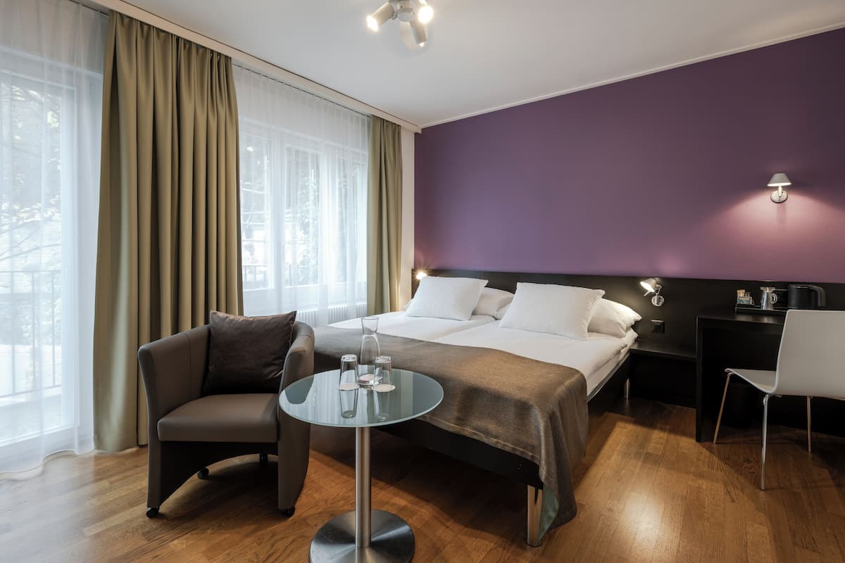 A hotel room with a bed, a chair, a small table, and a nightstand.