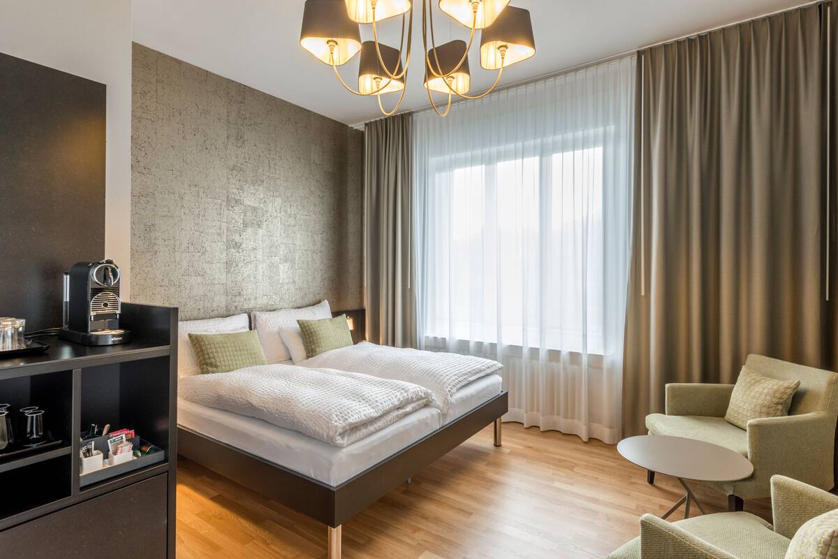 A modern hotel room with a large bed, a coffee machine, a small table, and a seating area.