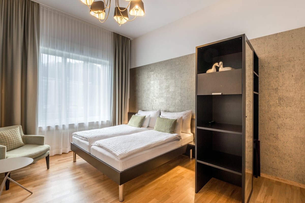A modern hotel room with a large bed, a desk, and a wardrobe.