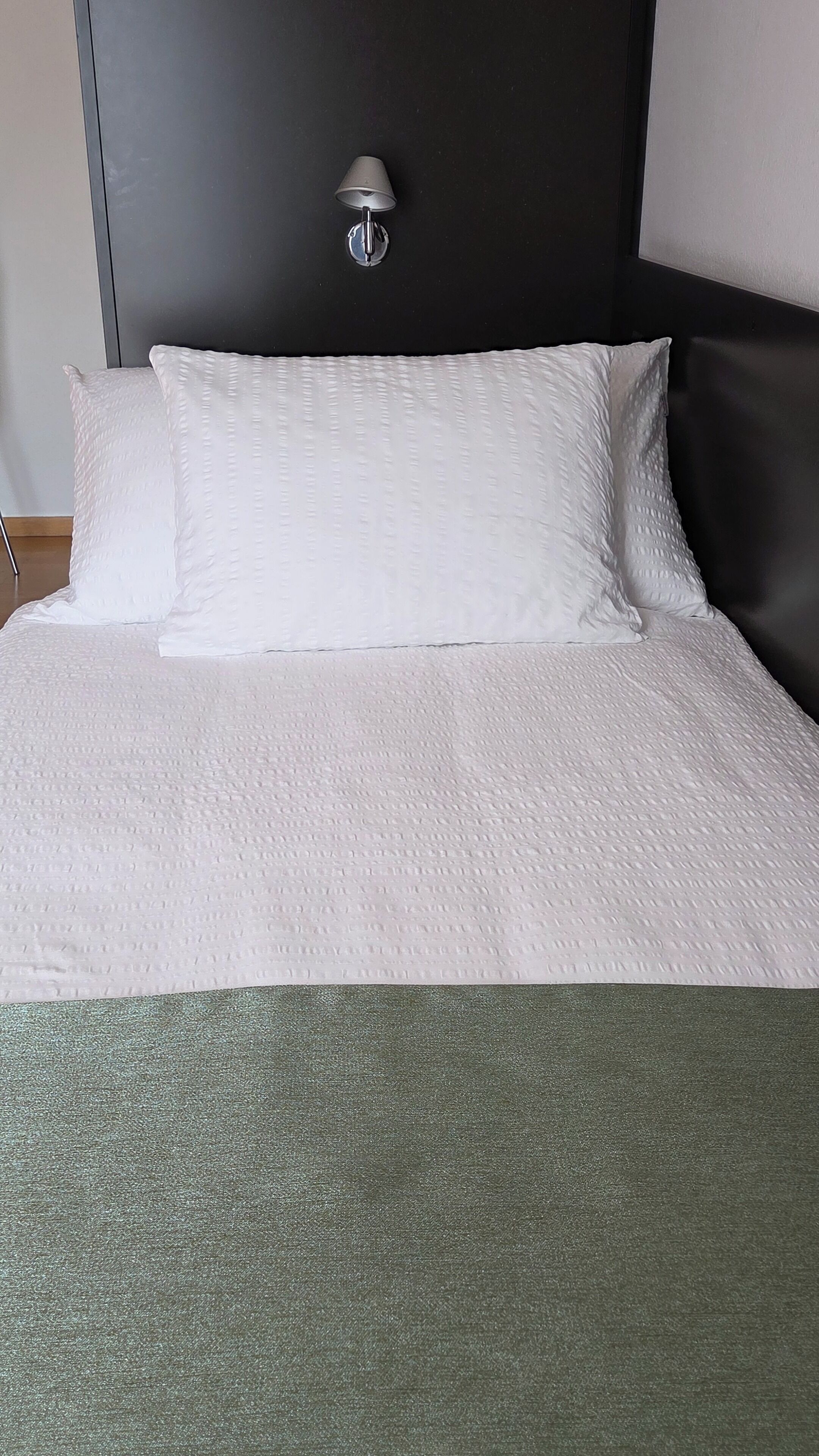 Una cama con ropa de cama blanca y un edredón verde.