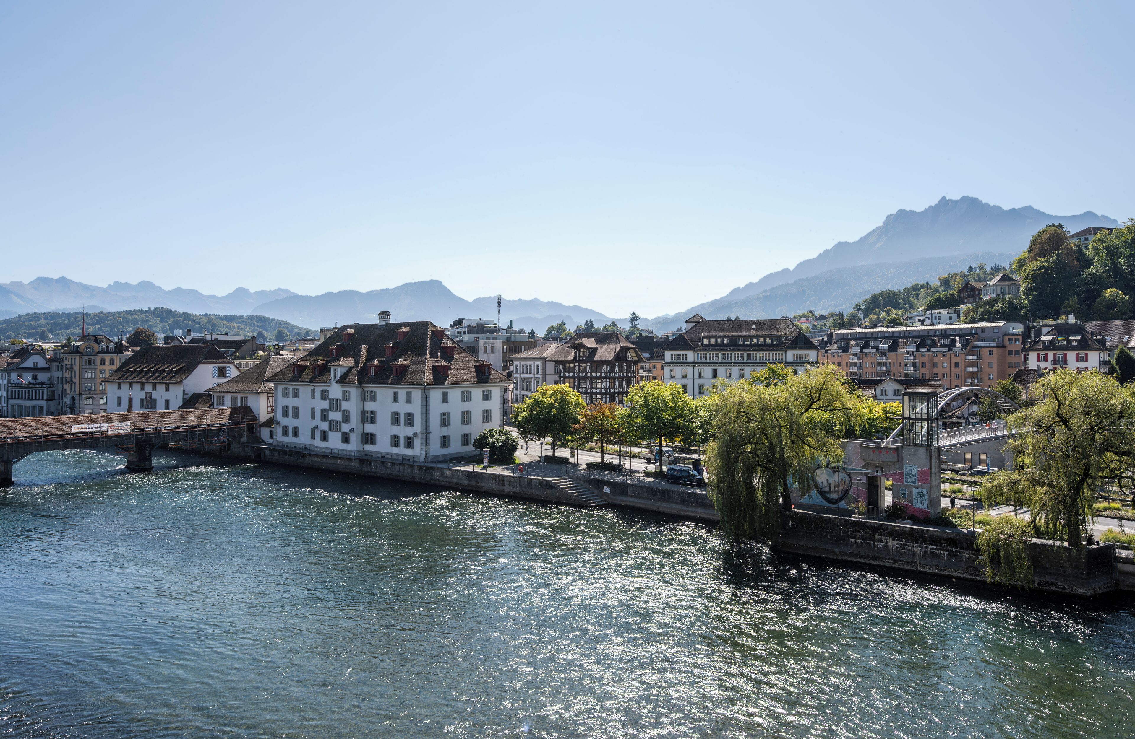A riverside town with historic buildings, a bridge, and mountains in the background.