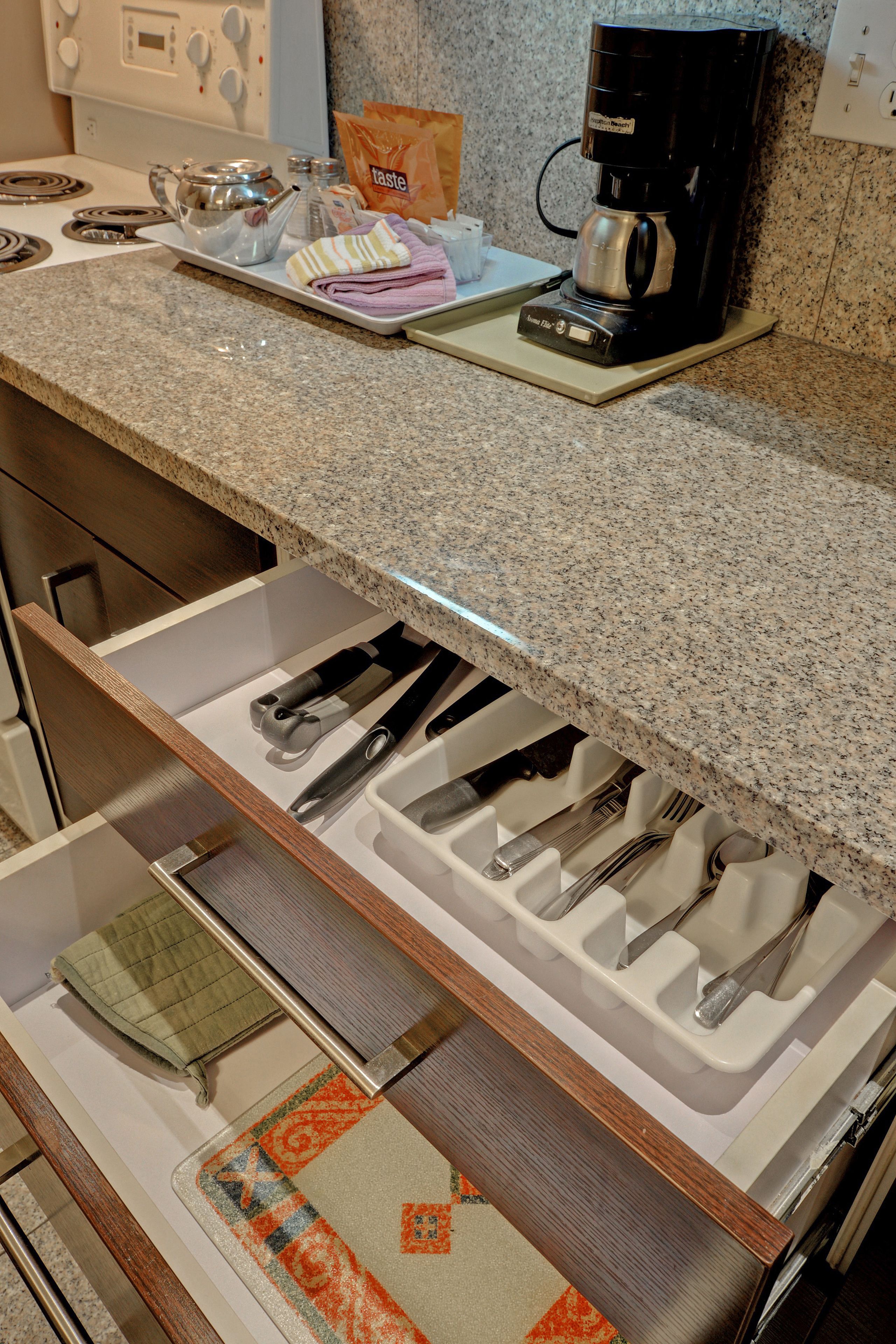 Una cocina con encimera de granito, cafetera y organizador de cajones con utensilios.