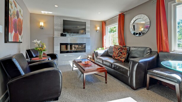 A modern living room with a fireplace, leather sofas, a flat-screen TV, and a glass coffee table.