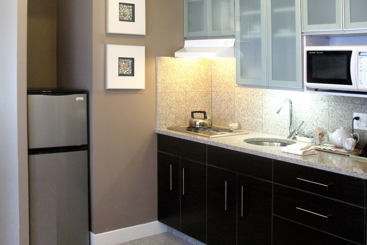 A compact kitchen with a refrigerator, microwave, sink, and dark cabinets.