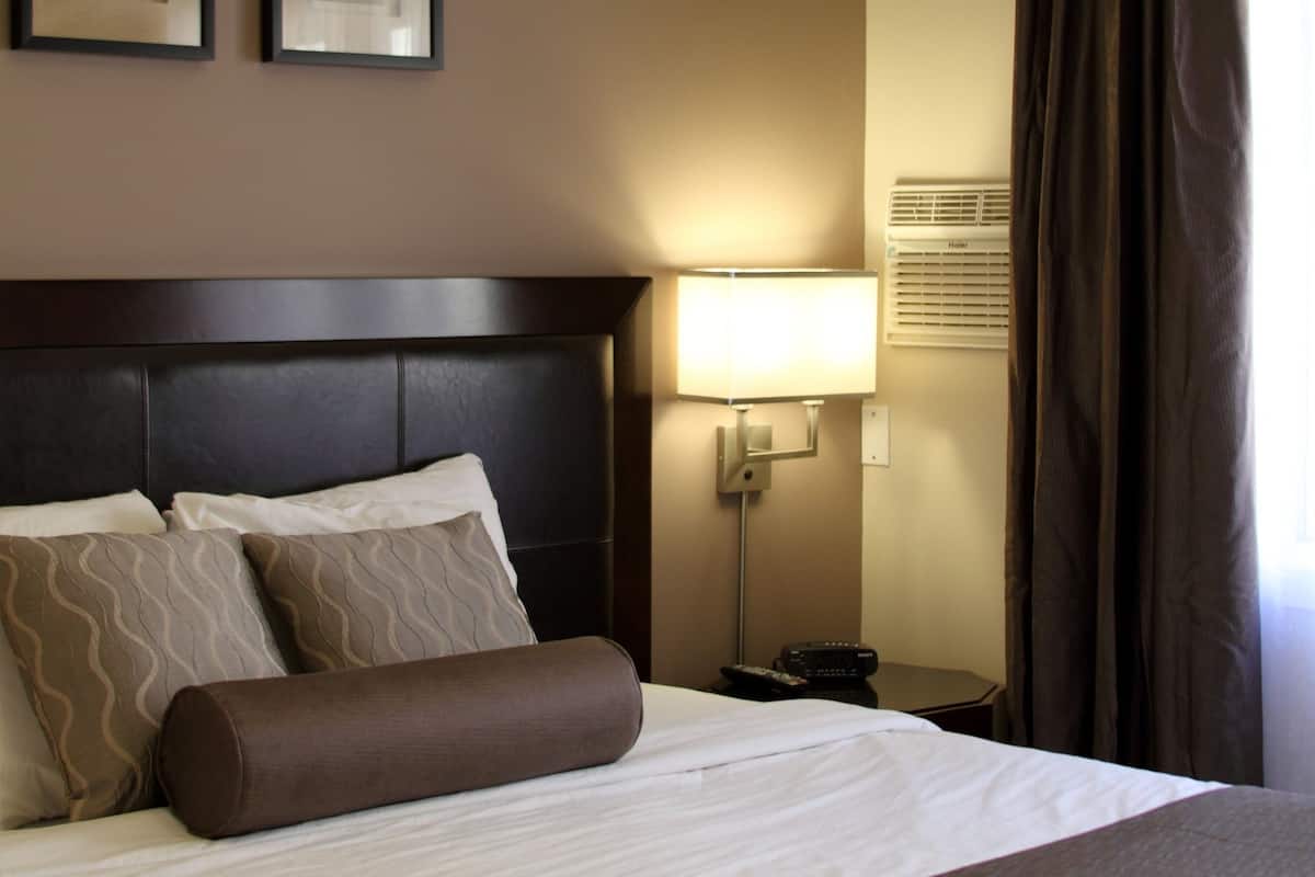 A neatly made bed with a headboard, a bedside lamp, and two framed pictures on the wall.