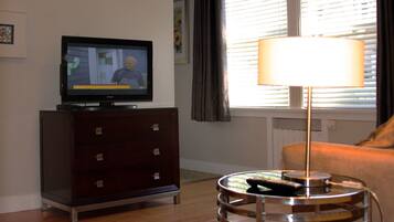 A living room with a TV on a cabinet, a lamp on a side table, and a window with blinds.